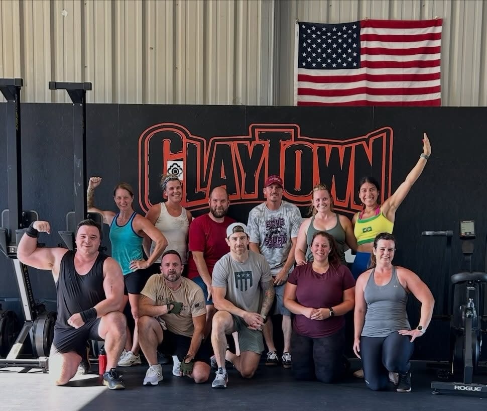 The Claytown CrossFit community in front of the gym logo wall